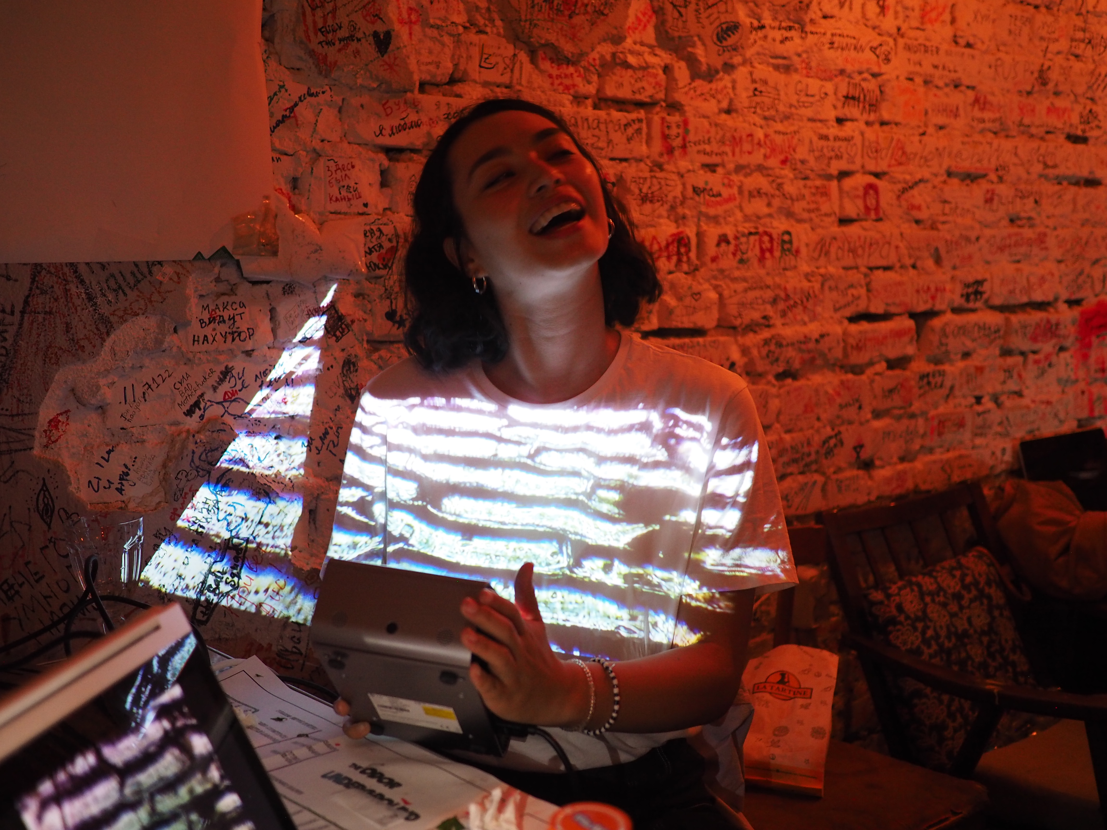 a woman smiling in a dimly lit room while an image of cells is projected onto her shirt